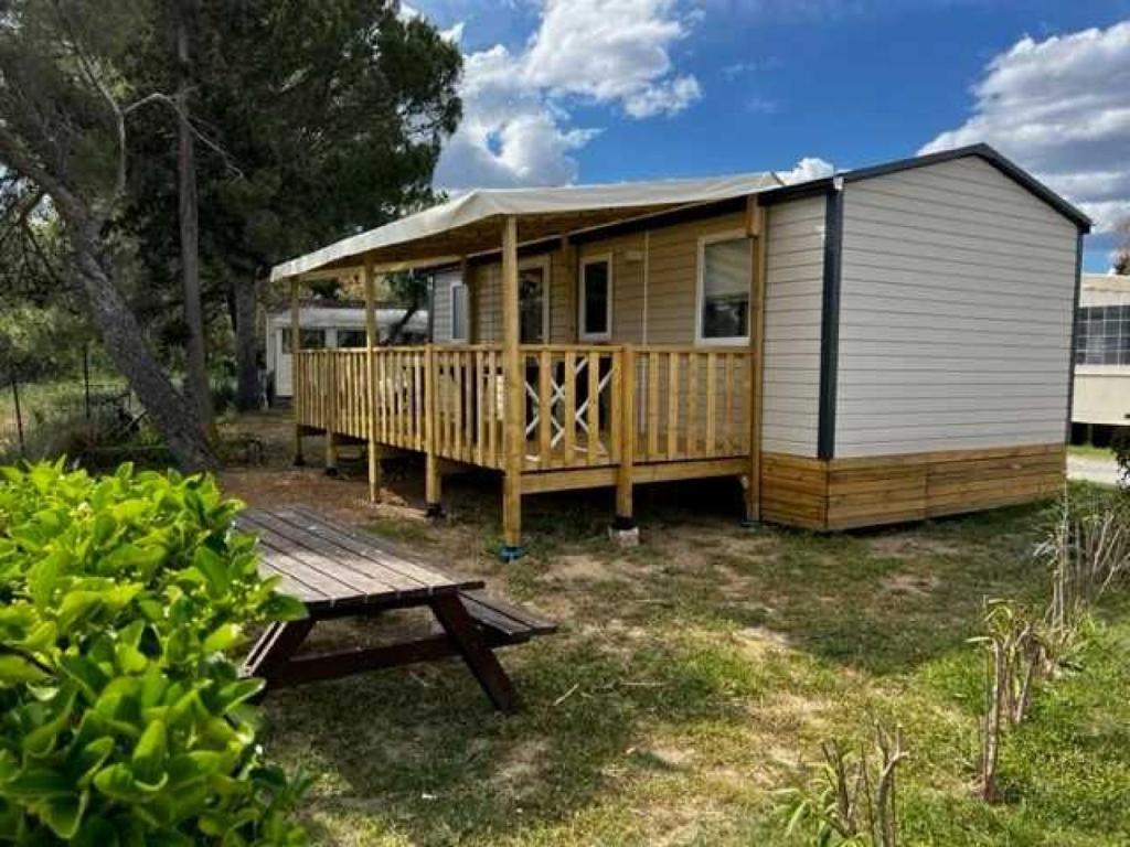 une petite maison avec une terrasse et une table de pique-nique dans l'établissement Camping 2 étoiles - Piscine - ccb0fdi, à Villeneuve-lès-Maguelone