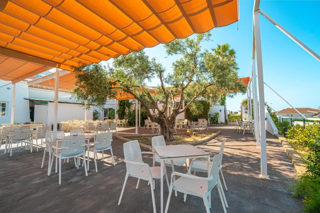 a patio with tables and chairs under an orange umbrella at Ohtels Carabela in Matalascañas