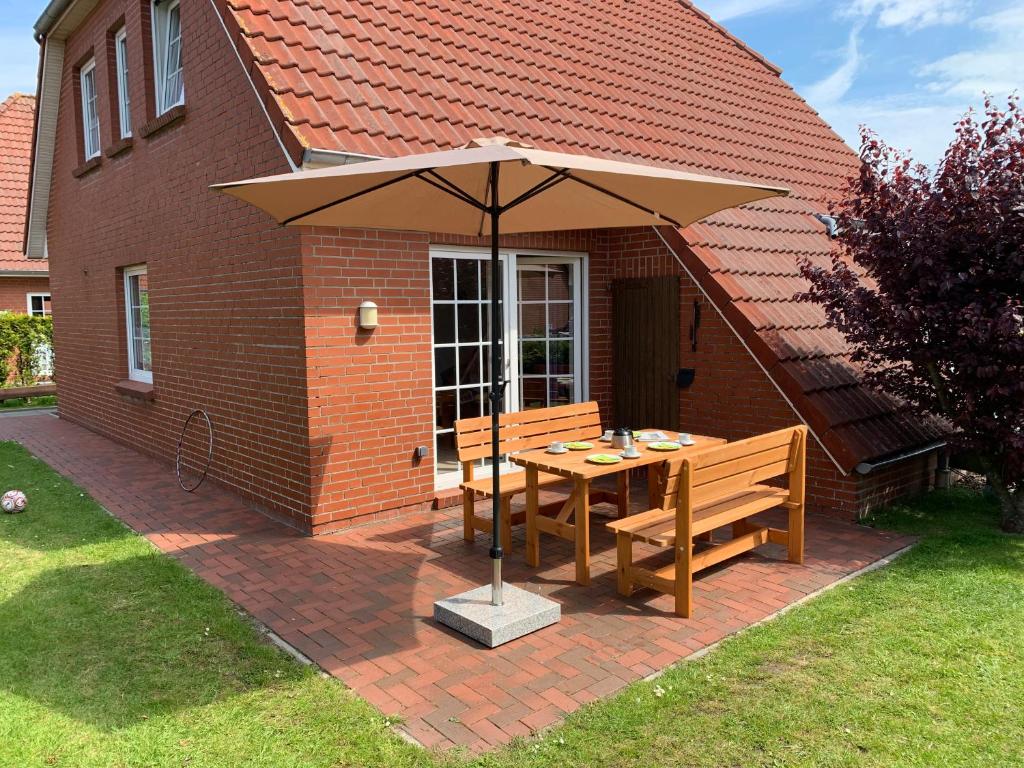 a patio with an umbrella and a table and benches at Ferienhaus Maren in Nessmersiel an der Nordsee - hochwertig und gemütlich in Dornum