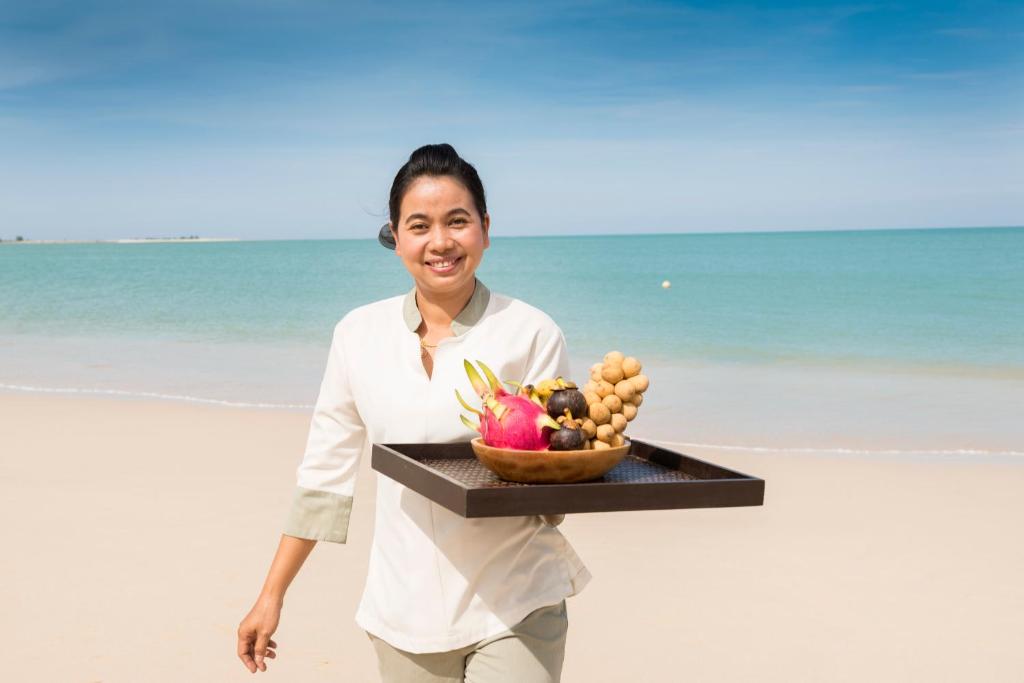 a woman walking on the beach holding a tray of fruit at The Sarojin in Khao Lak