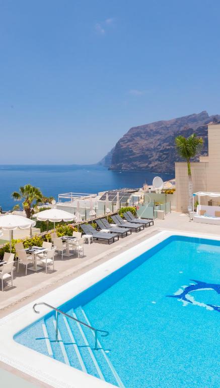 Una piscina con sillas y sombrillas y el océano. en Klayman Diamond Aparthotel, en Acantilado de los Gigantes