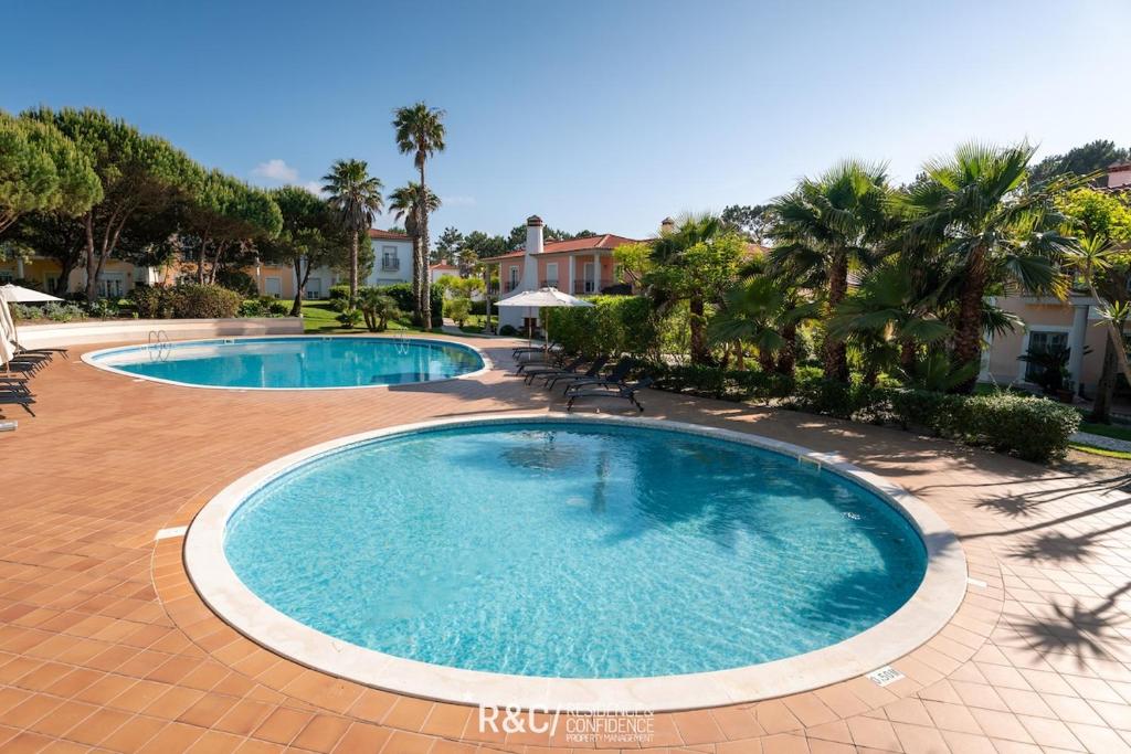 two swimming pools in a courtyard with palm trees at Casa da Isla - Praia del Rey Golf & Beach Resort in Amoreira