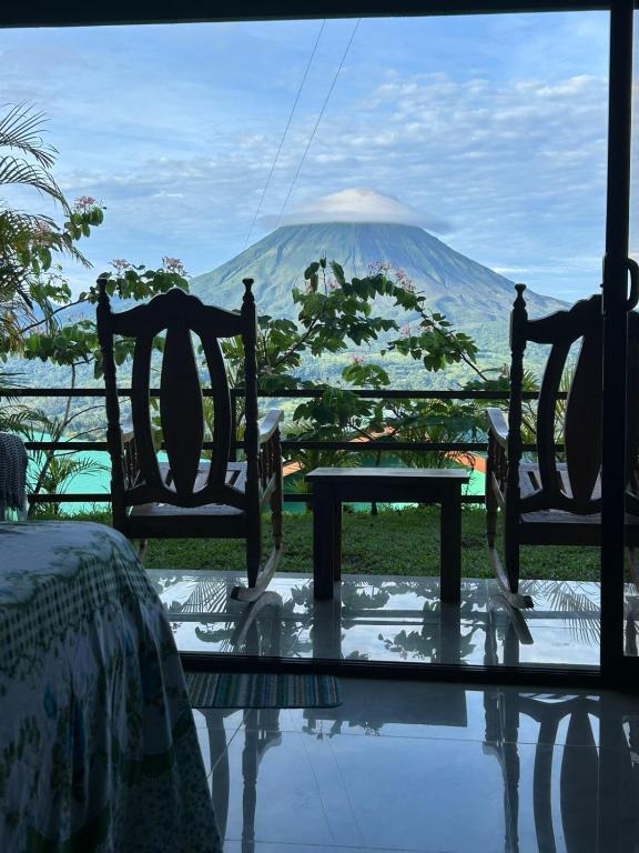 a room with two chairs and a table and a mountain at Encanto Arenal lodge in Fortuna