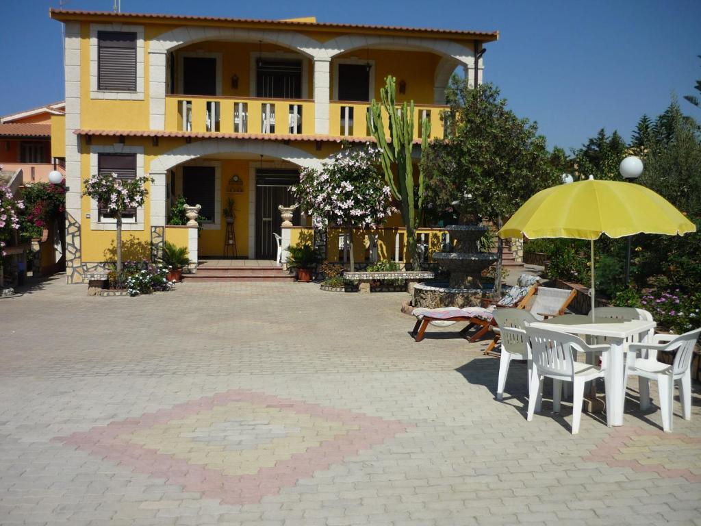 uma casa amarela com mesas e cadeiras e um guarda-sol em Villa Pisciotto em Licata