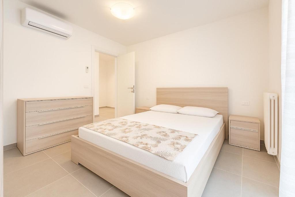 Un dormitorio blanco con una cama grande y una ventana. en Garden apartment with parking, en Lignano Sabbiadoro