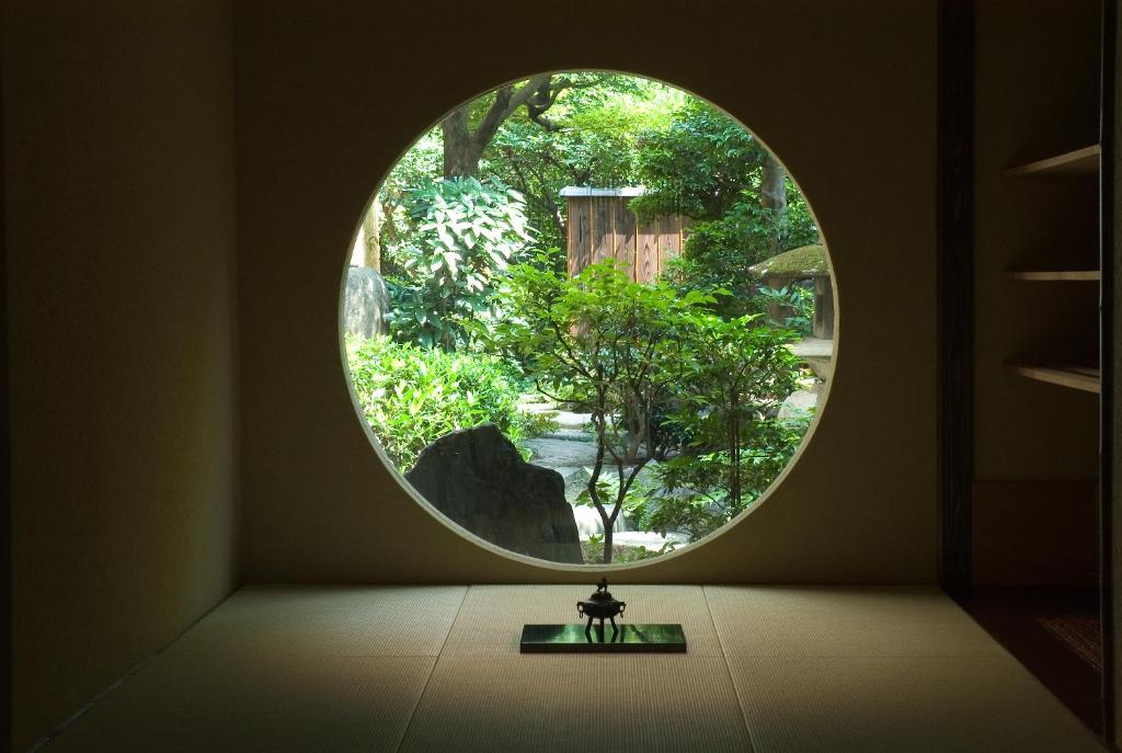 una ventana redonda en una habitación con una mesa con reloj en Yadoya Nishijinso en Kioto