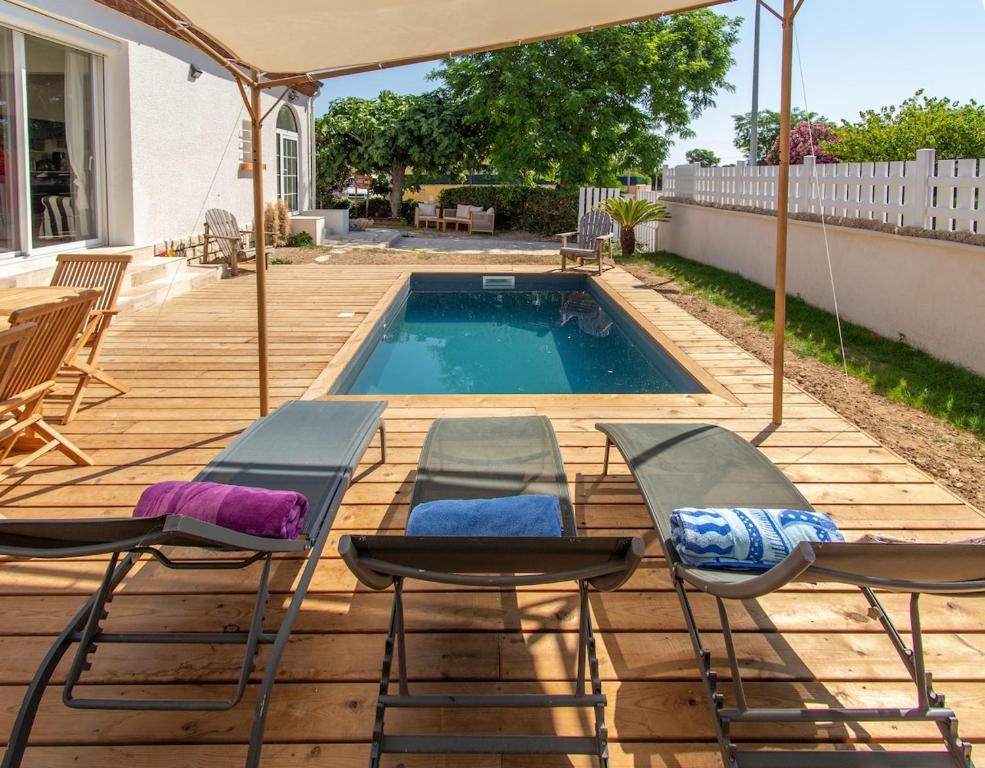 einen Pool mit Stühlen und einem Sonnenschirm auf einer Holzterrasse in der Unterkunft Somptueuse villa piscine terrain de pétanque à 10 min de Sète in Frontignan