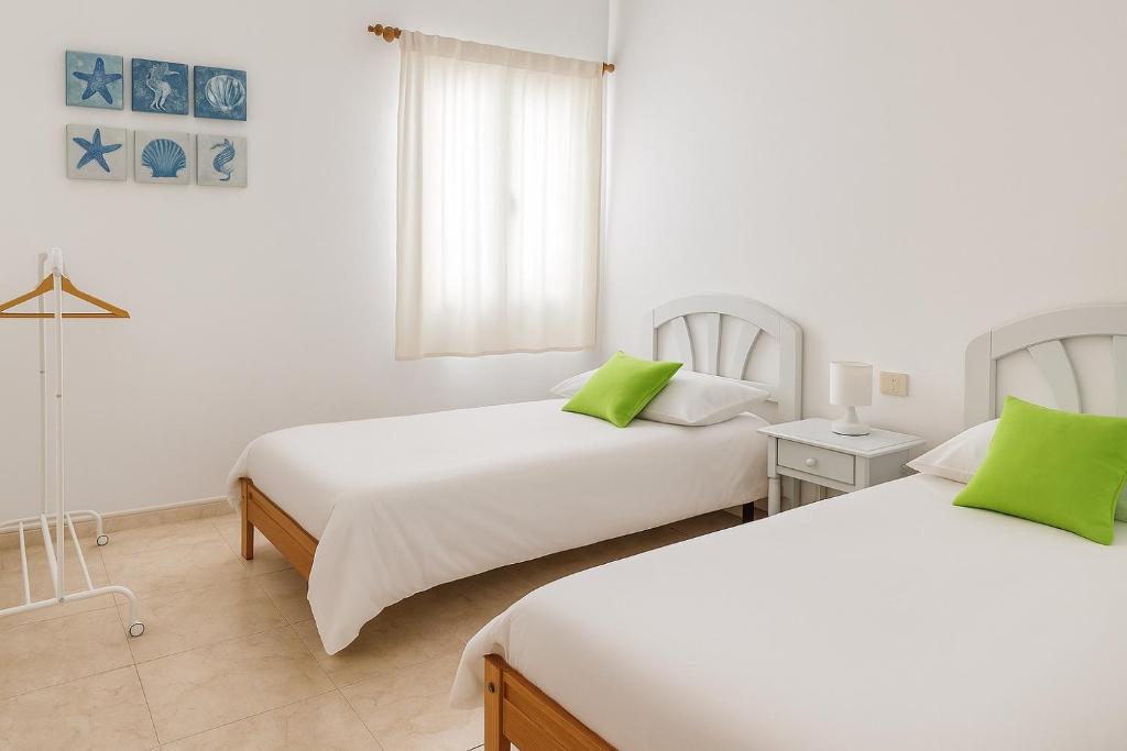 two beds in a white room with green pillows at Casa Brisa in La Santa