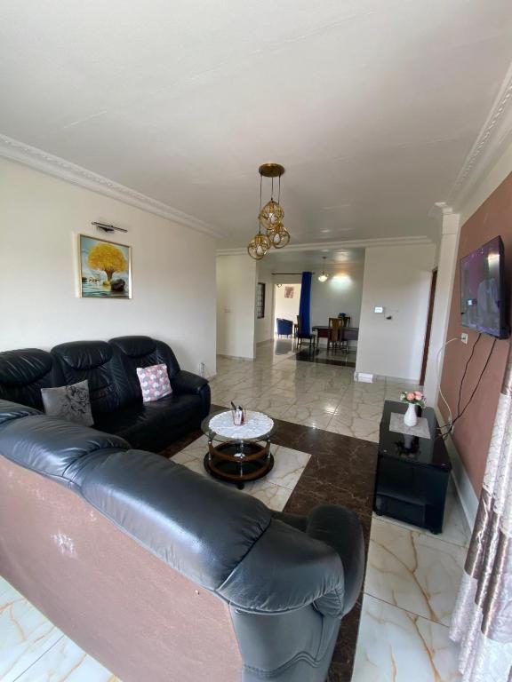 a living room with a black leather couch and a table at Appartement meublé spacieux 2 chambres salon Yassa in Douala