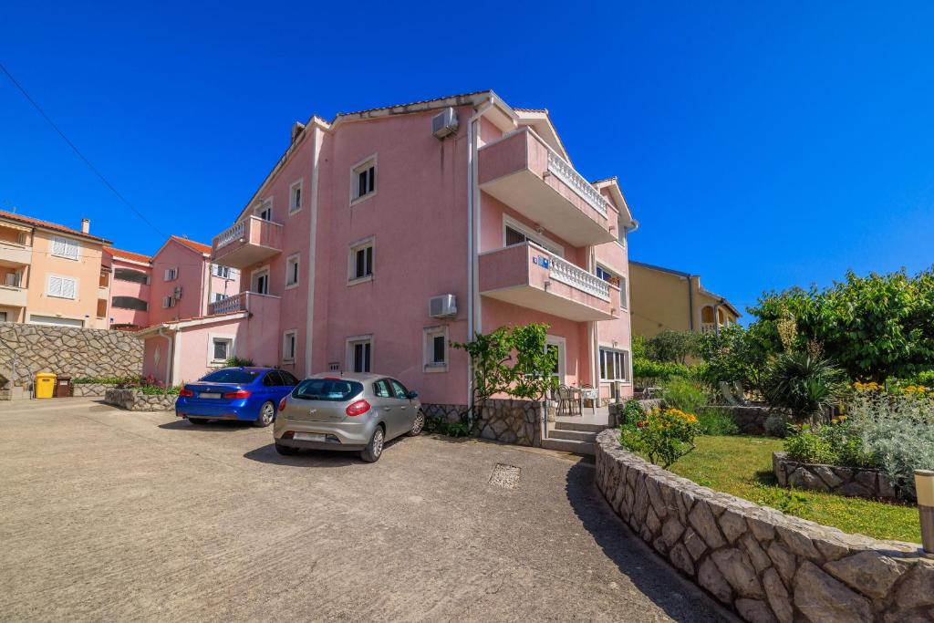 a pink building with cars parked in a parking lot at Apartments Krunoslav in Punat