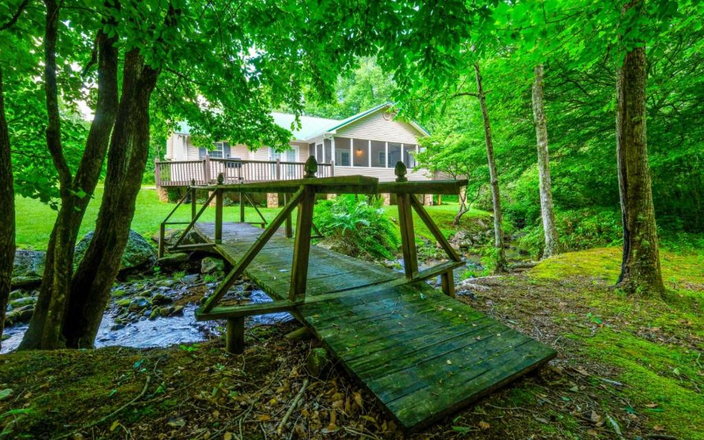 ein Haus im Wald mit einer Brücke über einen Fluss in der Unterkunft Hen Wallow Creek Cottage in Cosby