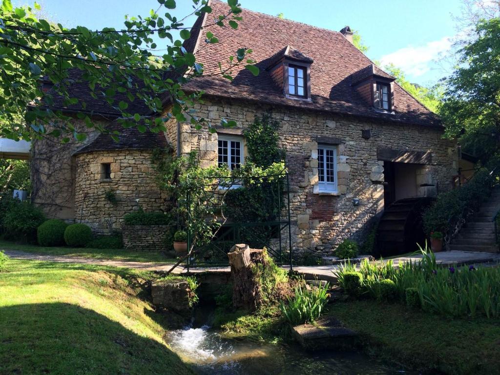 an old stone house with a stream in front of it at Le Moulin De La Beune in Les Eyzies-de-Tayac