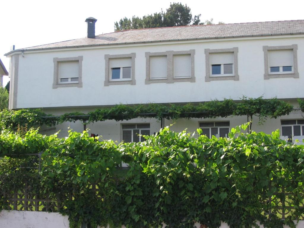 a white house with green trees in front of it at Pensión Portomiño in Portomarin