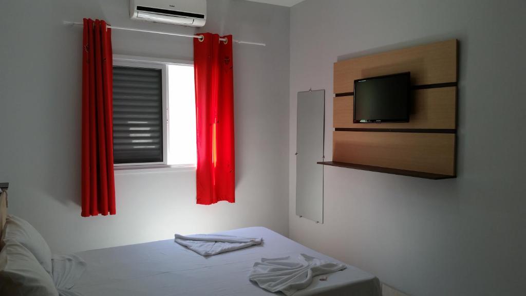 um quarto com uma cama e uma janela com cortinas vermelhas em Hotel Cavalo Marinho Suítes em Caraguatatuba