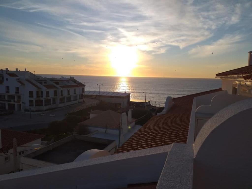 a sunset over the ocean from the roofs of buildings at Casa Melli with Sunset Oceanview Terrace in Lourinhã
