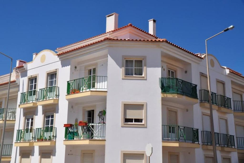 a white building with green balconies and a blue sky at Casa Anabela - Beach Apartment in Lourinhã