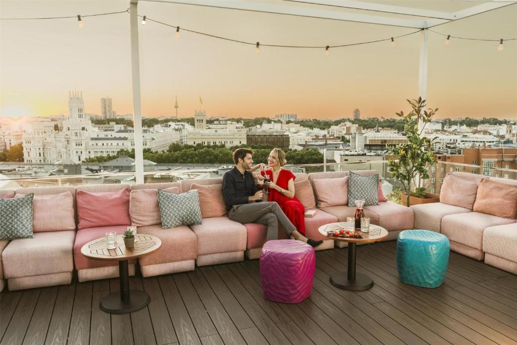 a man and woman sitting on a couch on a rooftop at NH Collection Madrid Suecia in Madrid