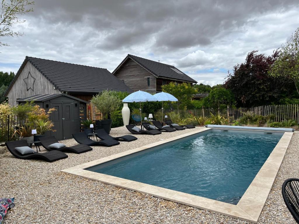 une piscine avec chaises et parasols devant une maison dans l'établissement Le Gîte du Puit des Granges, à Fontaine-sur-Coole