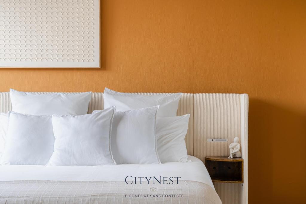 - un lit avec des oreillers blancs et un mur orange dans l'établissement Suite Premium CityNest, à Strasbourg
