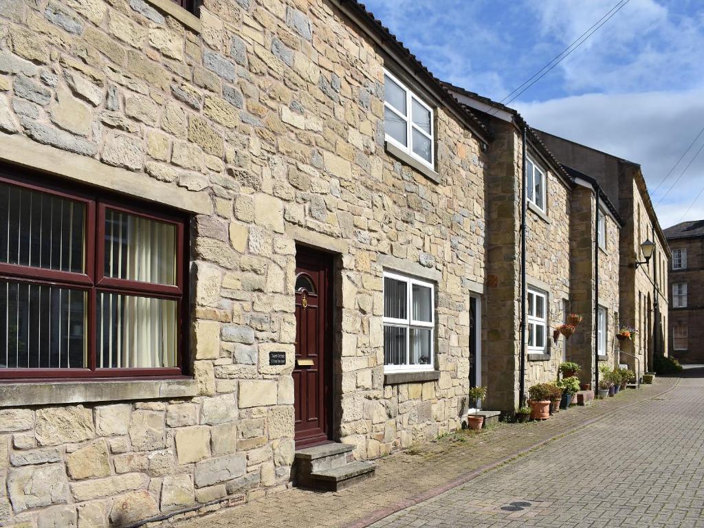 a stone building with a red door on a street at Twizell Cottage in Alnwick