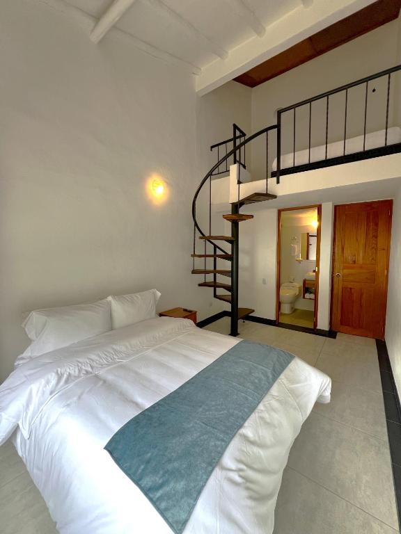 a bedroom with a white bed and a spiral staircase at Hotel Villa Macondo in Villa de Leyva