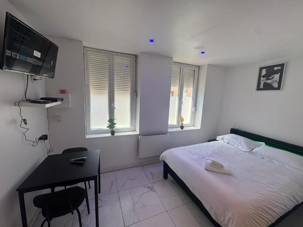 Un dormitorio con una cama y un escritorio y dos ventanas. en Royal appart city 1, en Calais