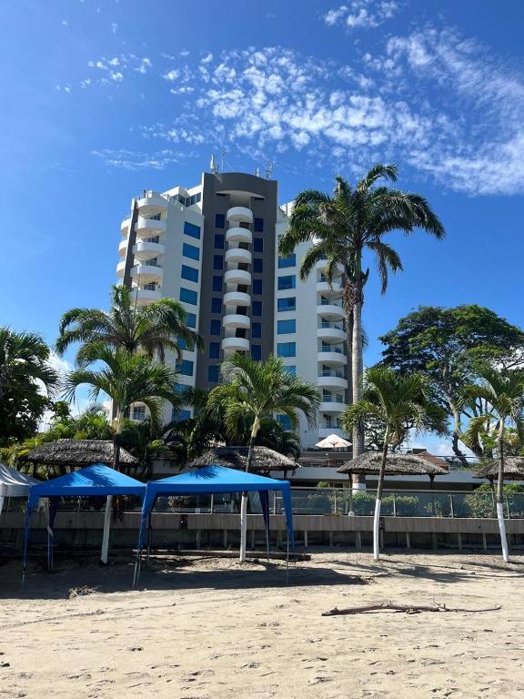 a building on the beach with palm trees and umbrellas at Penthouse frente al mar in Tonsupa