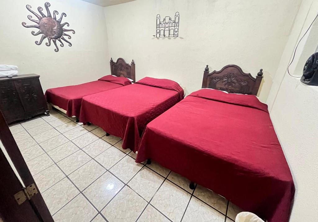three beds in a room with red sheets at Jireh guesthouse in Antigua Guatemala