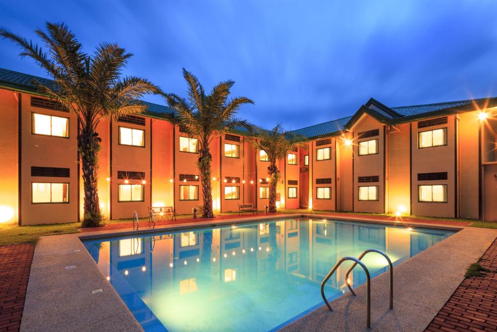 a swimming pool in front of a building with palm trees at Microtel by Wyndham Cabanatuan in Cabanatuan