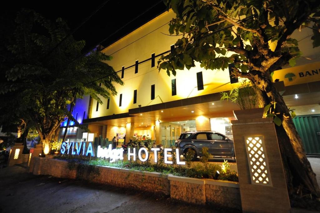 un hotel con un cartel delante de él por la noche en Sylvia Hotel Budget, en Kupang