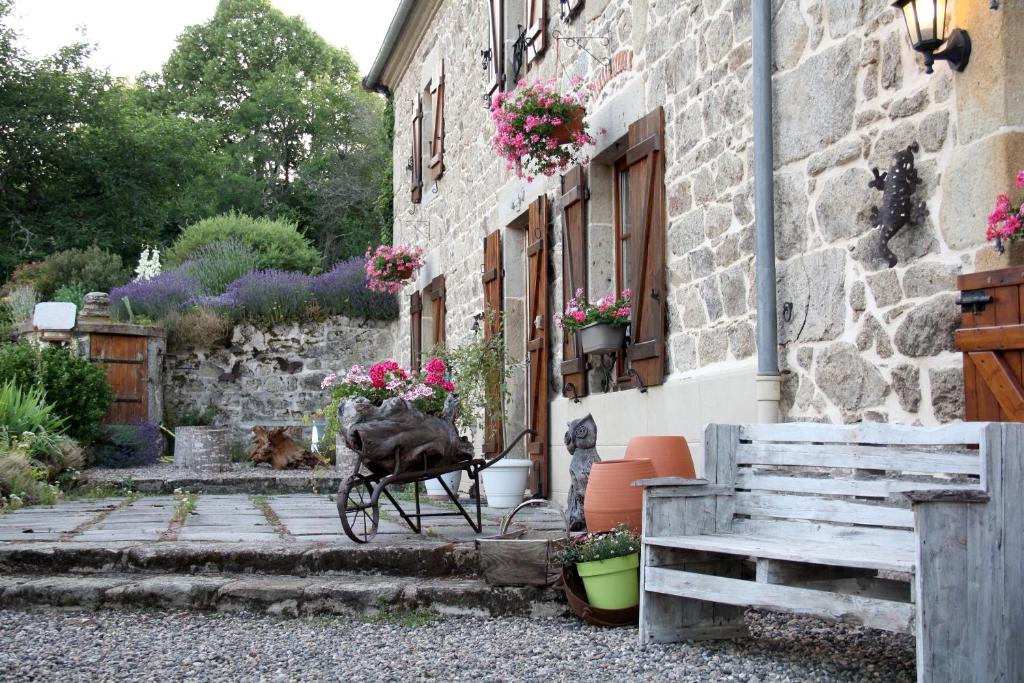 une maison en pierre avec une brouette ornée de fleurs dans l'établissement La Belle Âme, à Saint-Priest-des-Champs