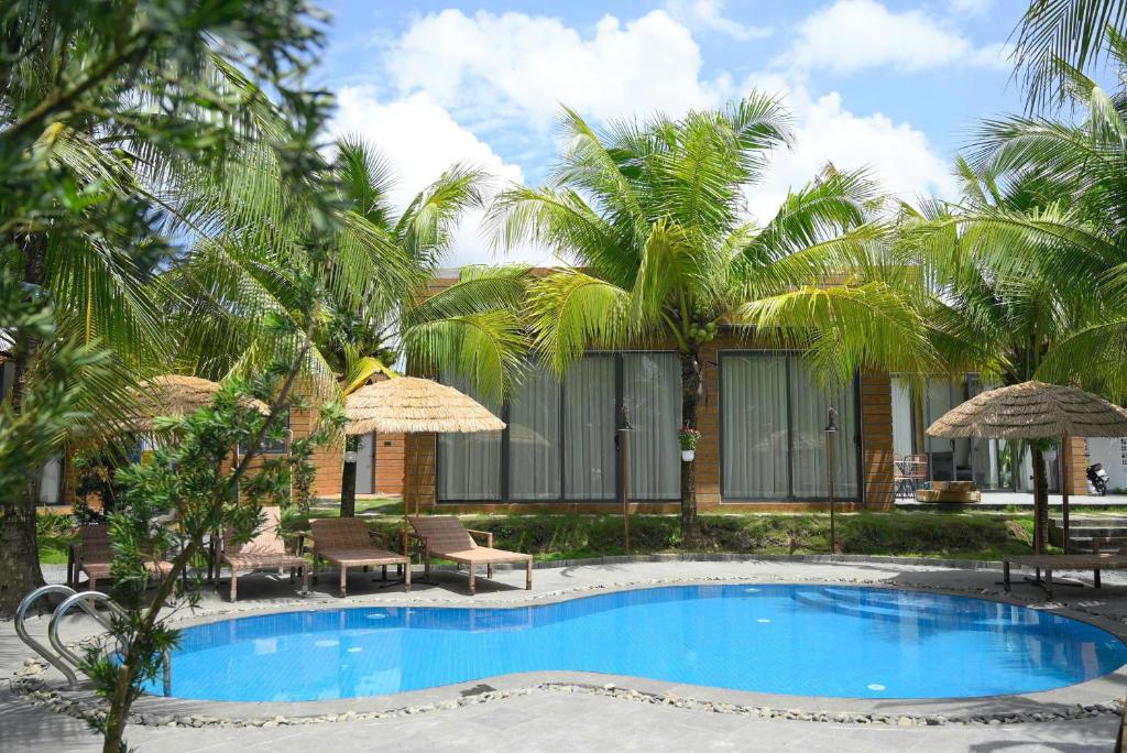 にあるBiển Tôm ốc Homestay - Hồ Bơi & BBQ Gardenのヤシの木が茂るリゾートの正面にあるスイミングプール