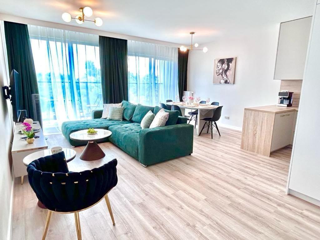 a living room with a green couch and a kitchen at Horyzont Apartamenty-Apartament Kaszmirowy Fale Bałtyku, sauna, siłownia, plac zabaw in Kołobrzeg