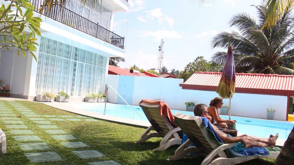 two people sitting in chairs next to a swimming pool at Ranga Holiday Resort in Bentota
