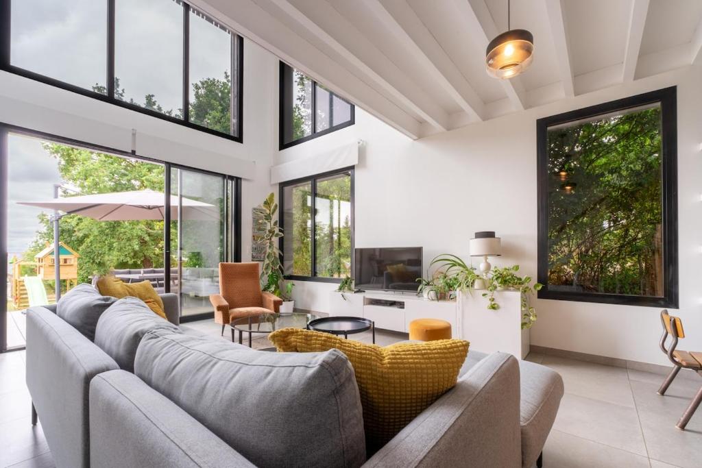a living room with a large couch and windows at Maison d'architecte au coeur de la nature in Guichen