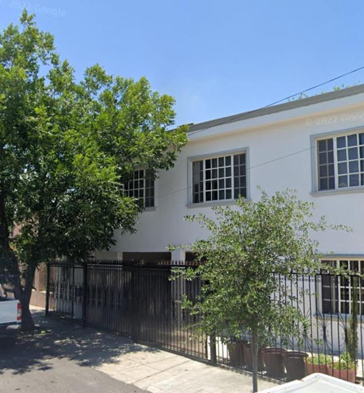 a white building with a black fence and trees at Depas Anahuac in Monterrey