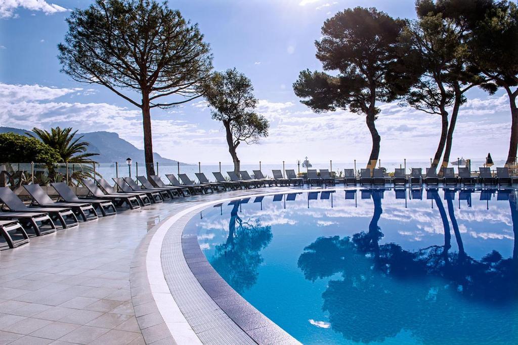 a swimming pool with chairs and trees on a building at Hôtel Vacances Bleues Delcloy in Saint-Jean-Cap-Ferrat