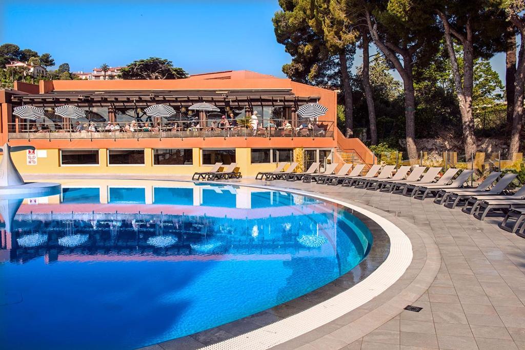 a large swimming pool with chairs and a building at Hôtel Vacances Bleues Delcloy in Saint-Jean-Cap-Ferrat