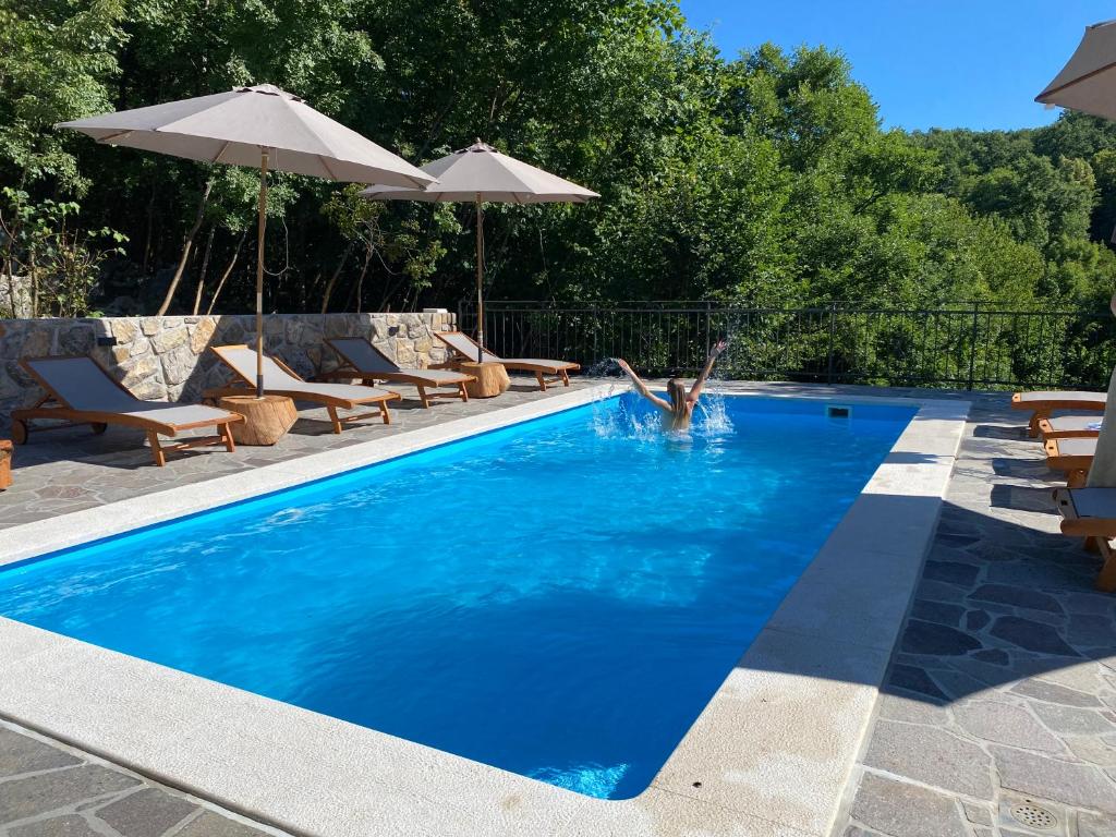 a pool with chairs and umbrellas and a person in the water at Familija Lovrinovi Retreat - Relax&Reconnect in Zvoneće