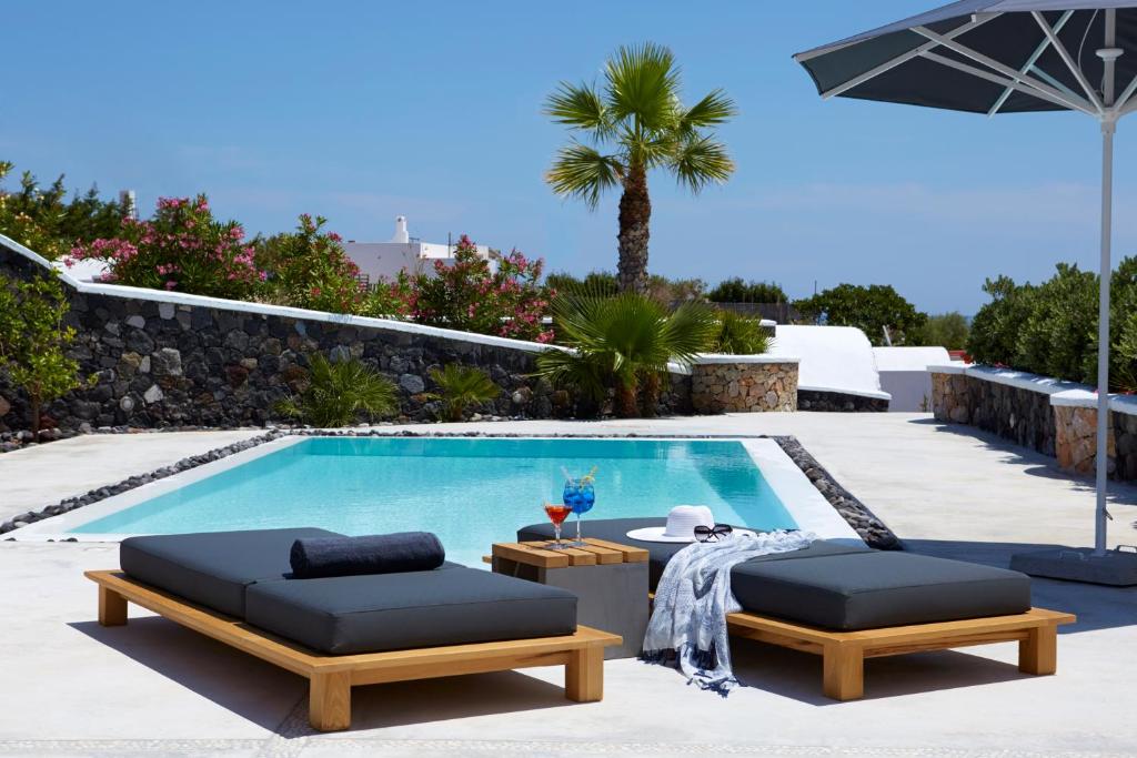 a swimming pool with two chairs and a table and an umbrella at Amor Hideaway Villas in Fira