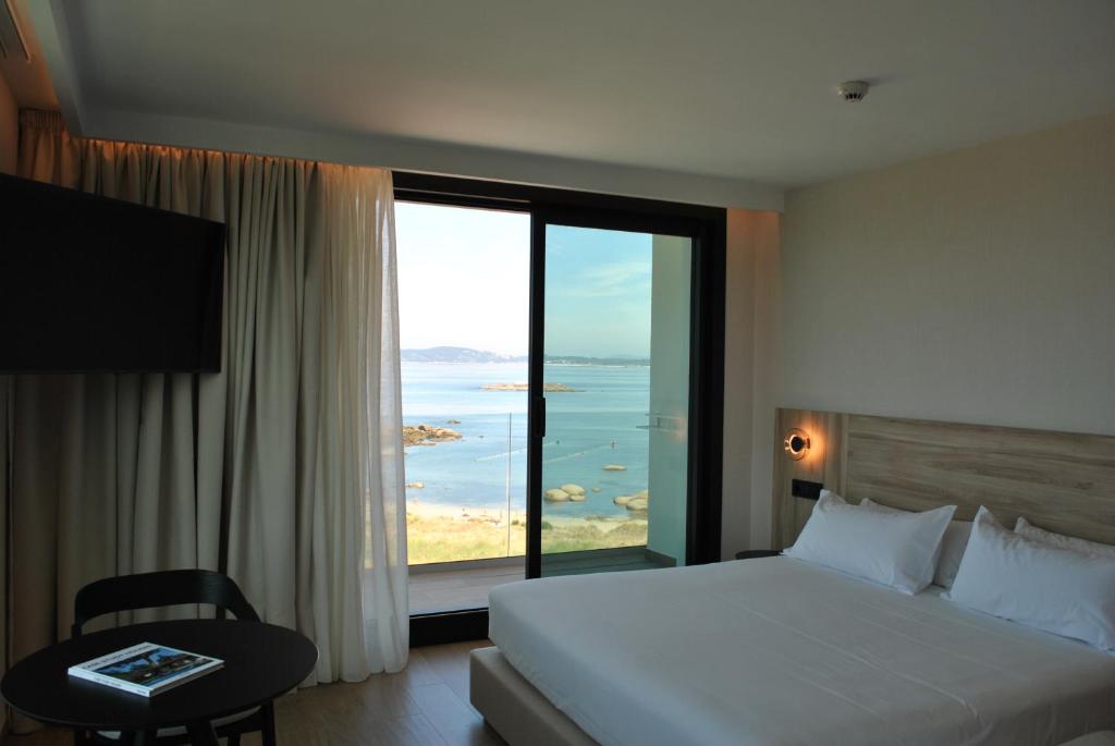 Una habitación de hotel con una cama y una ventana grande. en Hotel Delfin Azul, en A Lanzada