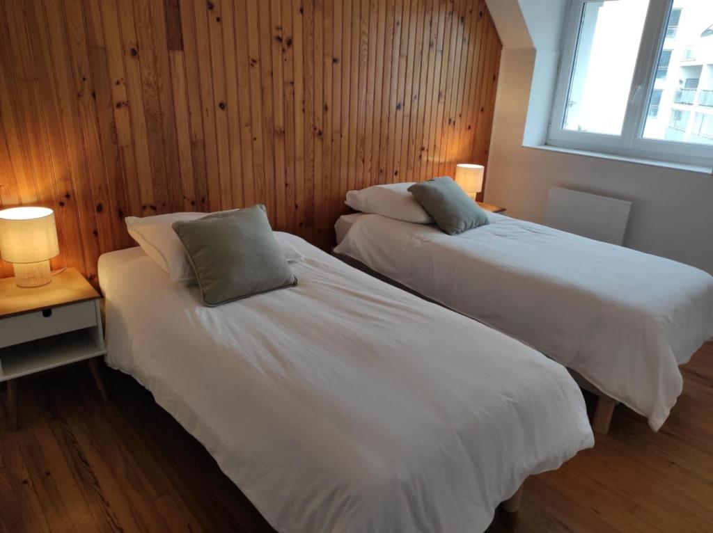 two beds in a room with wooden walls and a window at NOUVEAU YS EO, La maison sur le port de Tréboul in Douarnenez