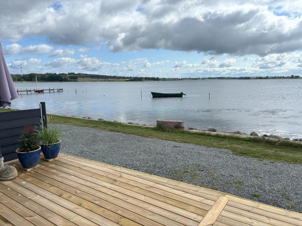 a wooden deck with a boat in the water at Feriebolig smukt beliggende i vandkanten in Munkebo