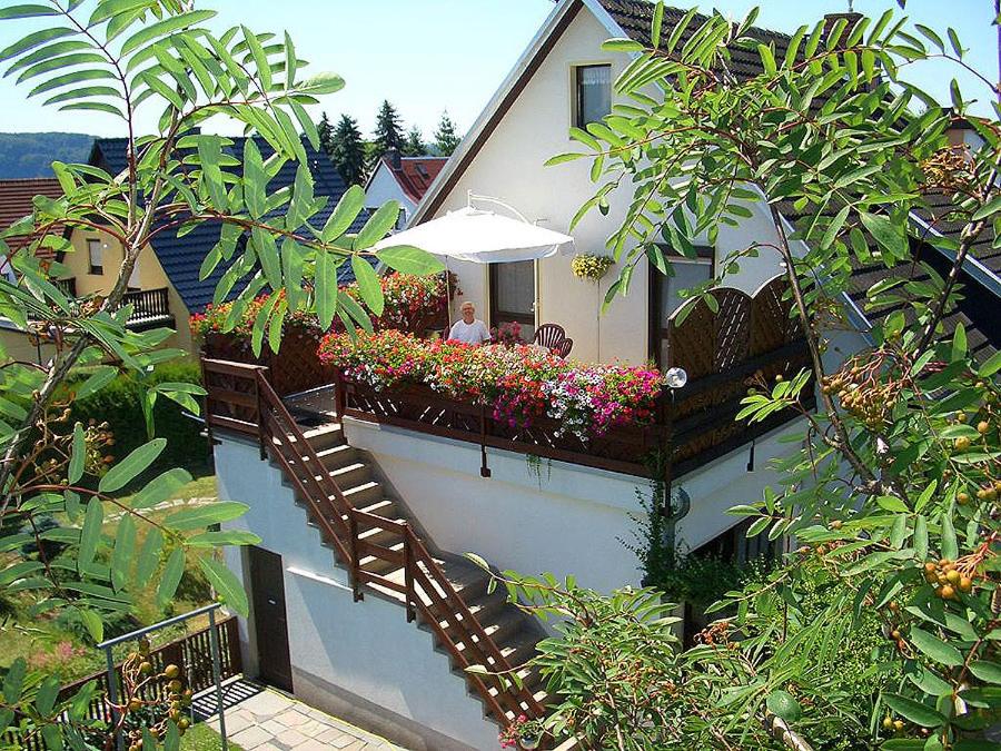 un balcón con mesa, sombrilla y flores en Haus König Ferienwohnung 1 und 2, en Lichtenhain