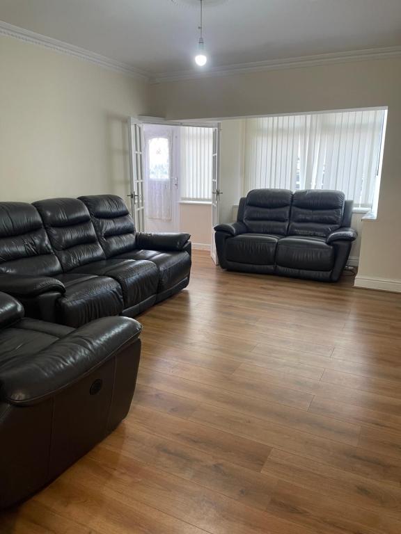 a living room with black leather furniture and wooden floors at Cleeve Road House in Birmingham