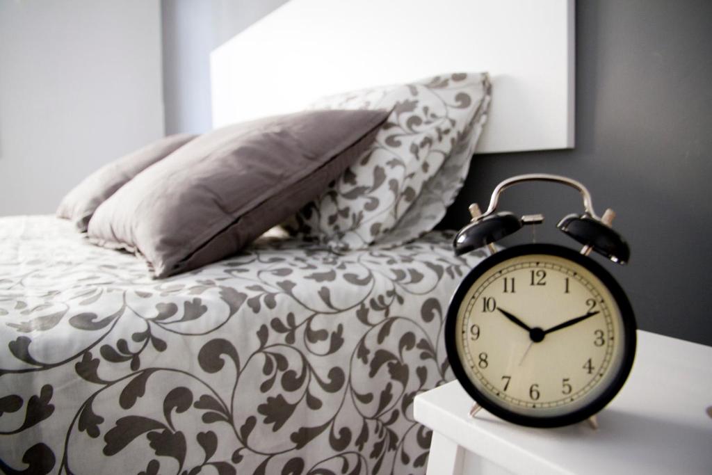 a clock on a table next to a bed with pillows at Apto. Santa Susanna in Santa Susanna