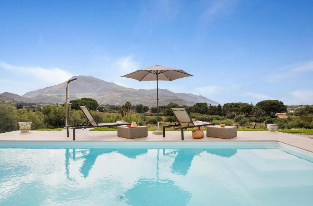 a swimming pool with two chairs and an umbrella at Historic Villa Overlooking Scopello Sea Stacks in Castellammare del Golfo