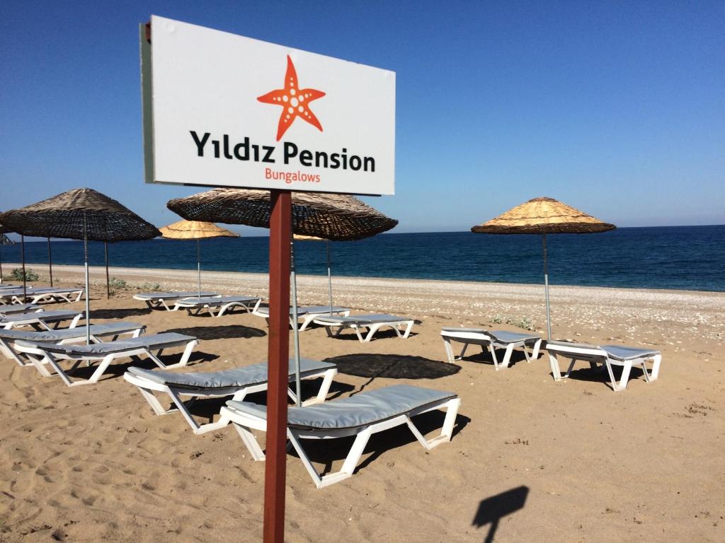 uma placa numa praia com cadeiras e guarda-sóis em Yildiz Pension Bungalows em Cirali