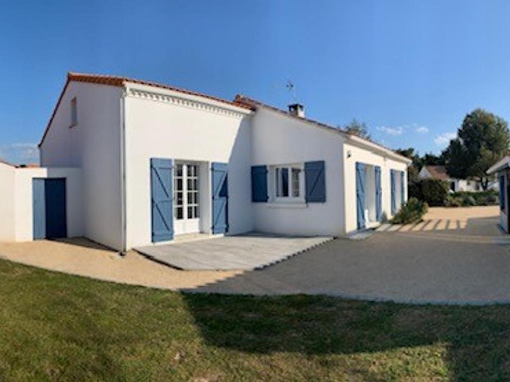 une maison blanche avec des portes bleues et une cour dans l'établissement Maison familiale à Notre-Dame-de-Monts - Plage à 600m, jardin, 3 chambres, confort moderne - FR-1-540-153, à Notre-Dame-de-Monts