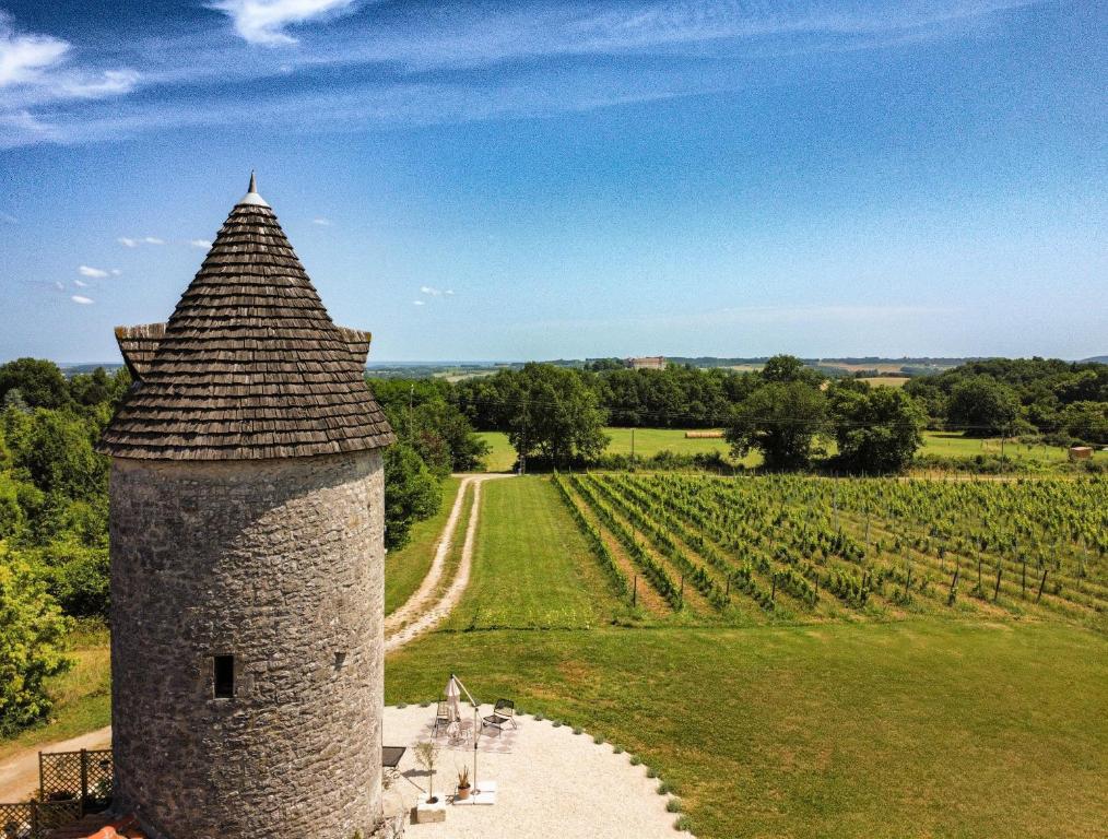 une tour de pierre dans un champ avec un vignoble dans l'établissement Toujours Dimanche Windmill Retreat, à Loubès-Bernac